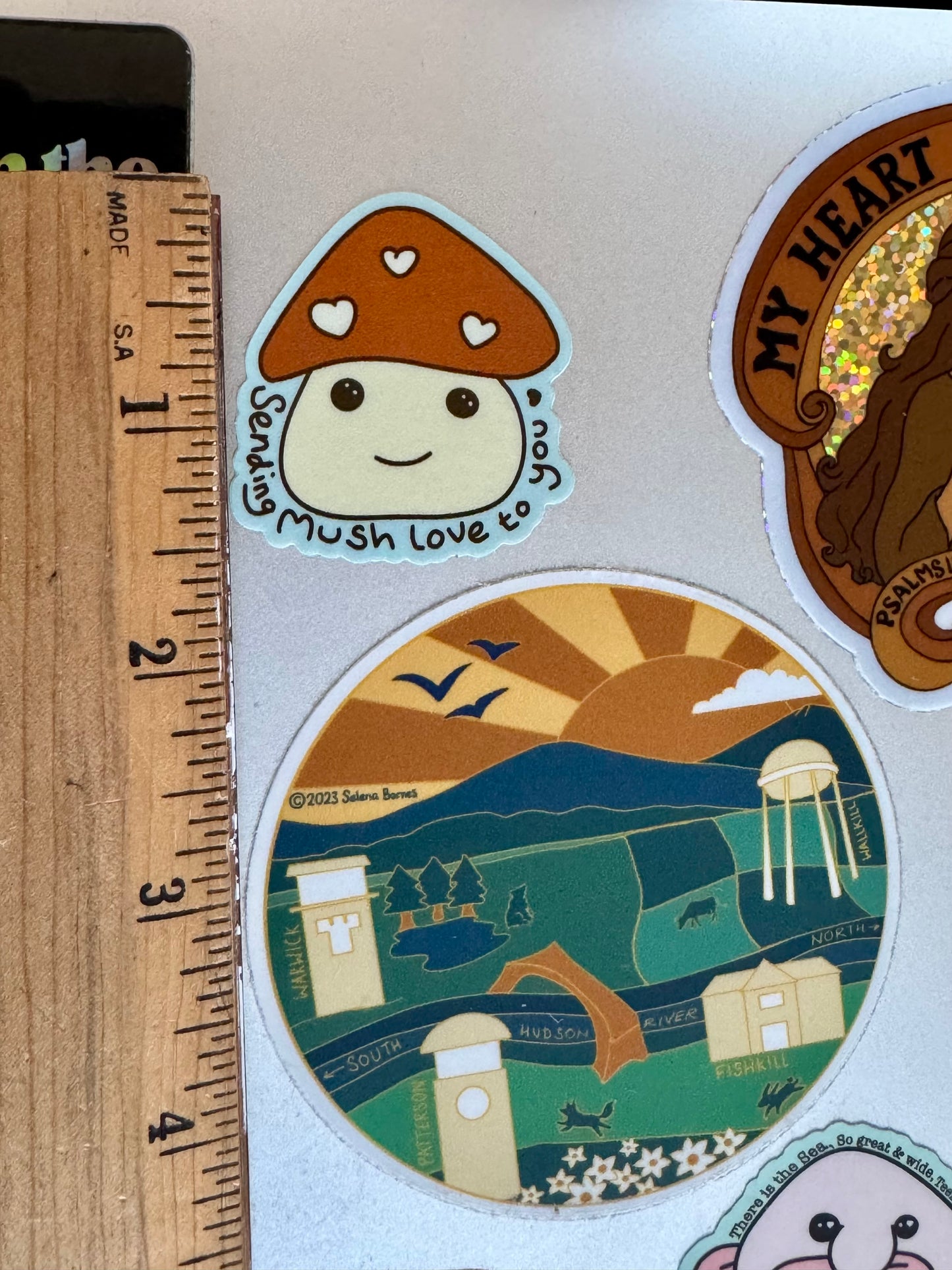 Sticker with a cartoon mushroom with a smily face next to a ruler for scale, showing it is 1 1/2" tall