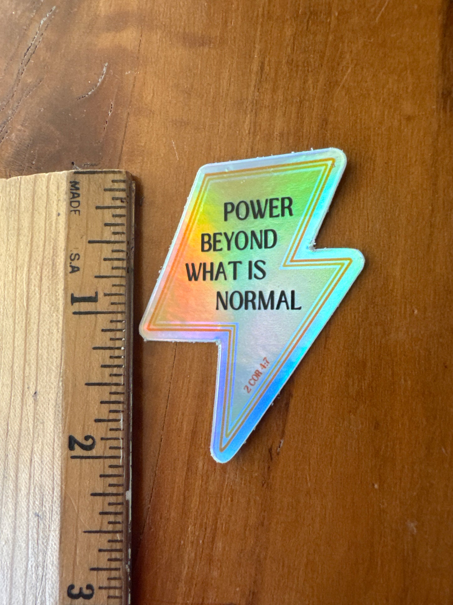 Holographic lightning sticker with a ruler for scale showing it is about 2" long
