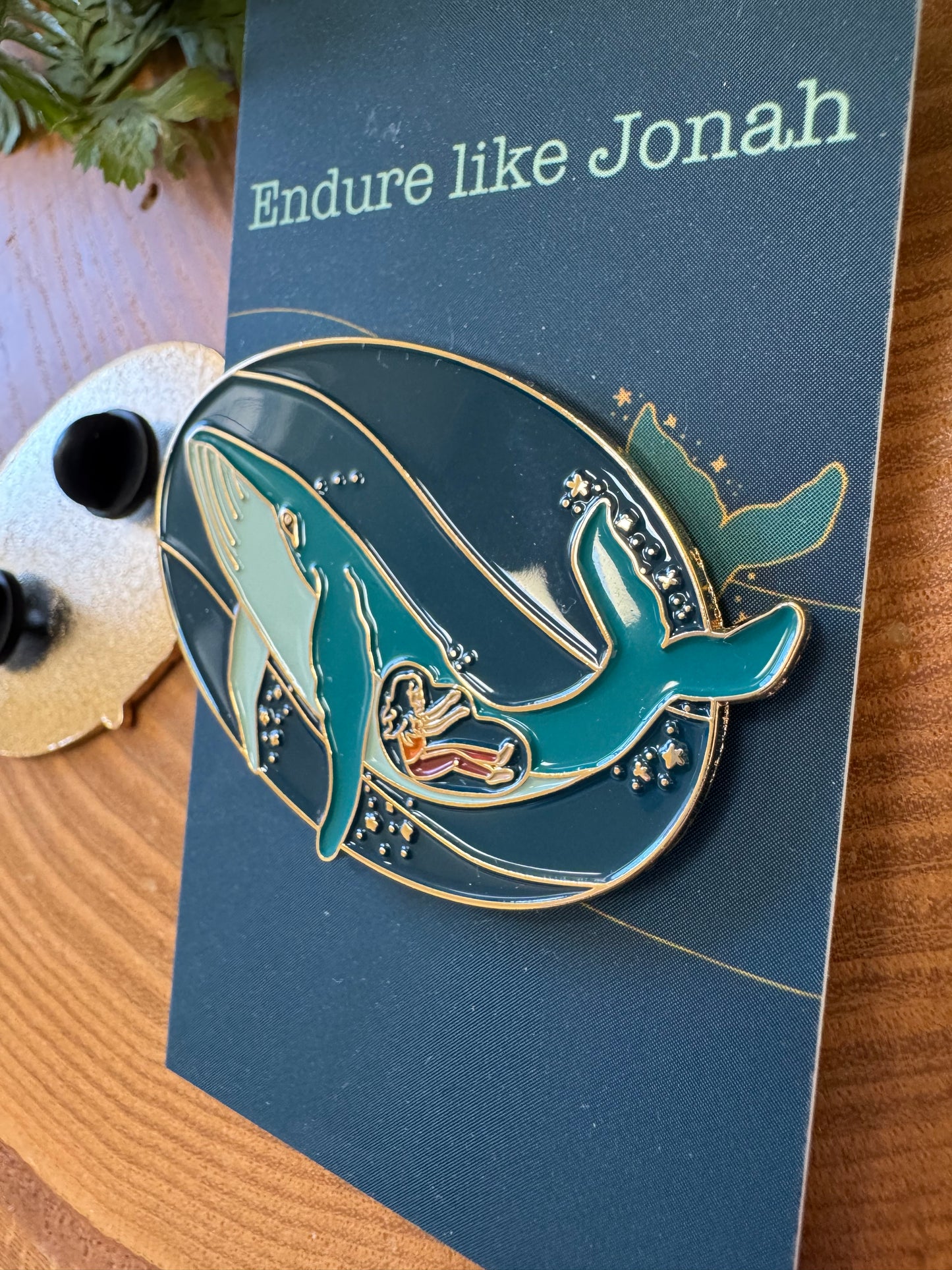 Blue pin of a whale on a backing card that says endure like jonah