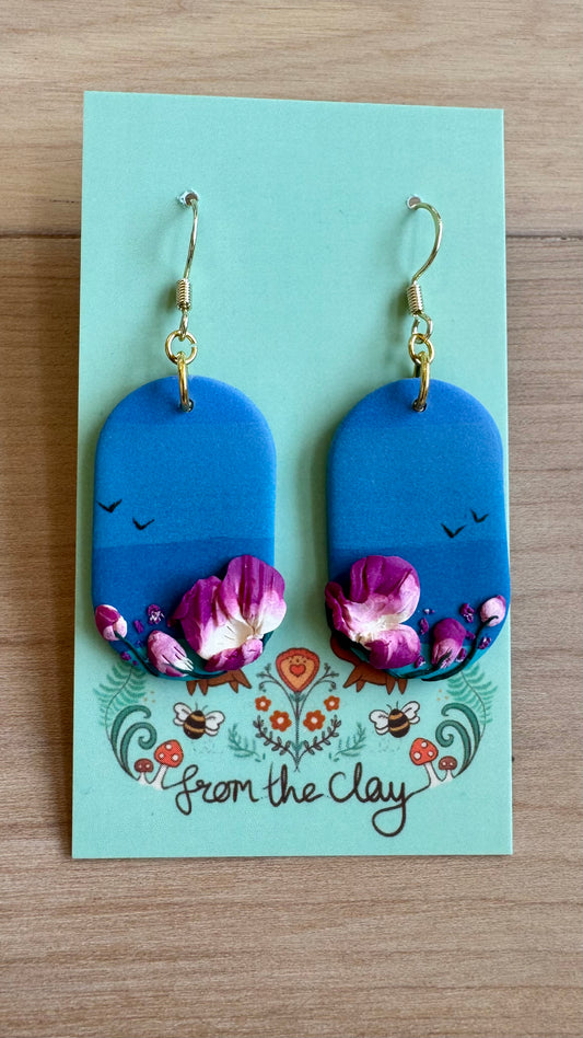 Blue earrings with floral design on a 'From the Clay' branded card.
