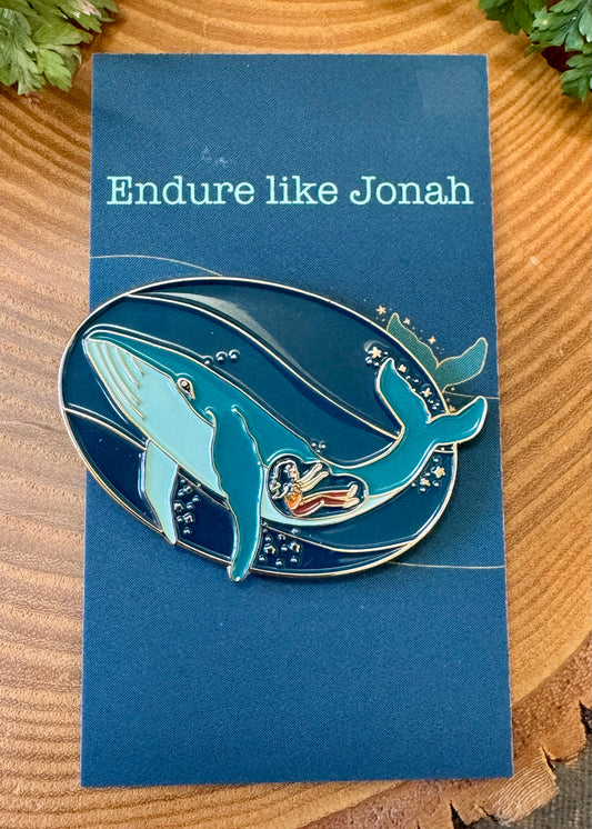 A pin and postcard set with an illustration of a whale and a person inside, titled 'Endure like Jonah'. The background is blue, and the text on the postcard reads the same as the illustration.