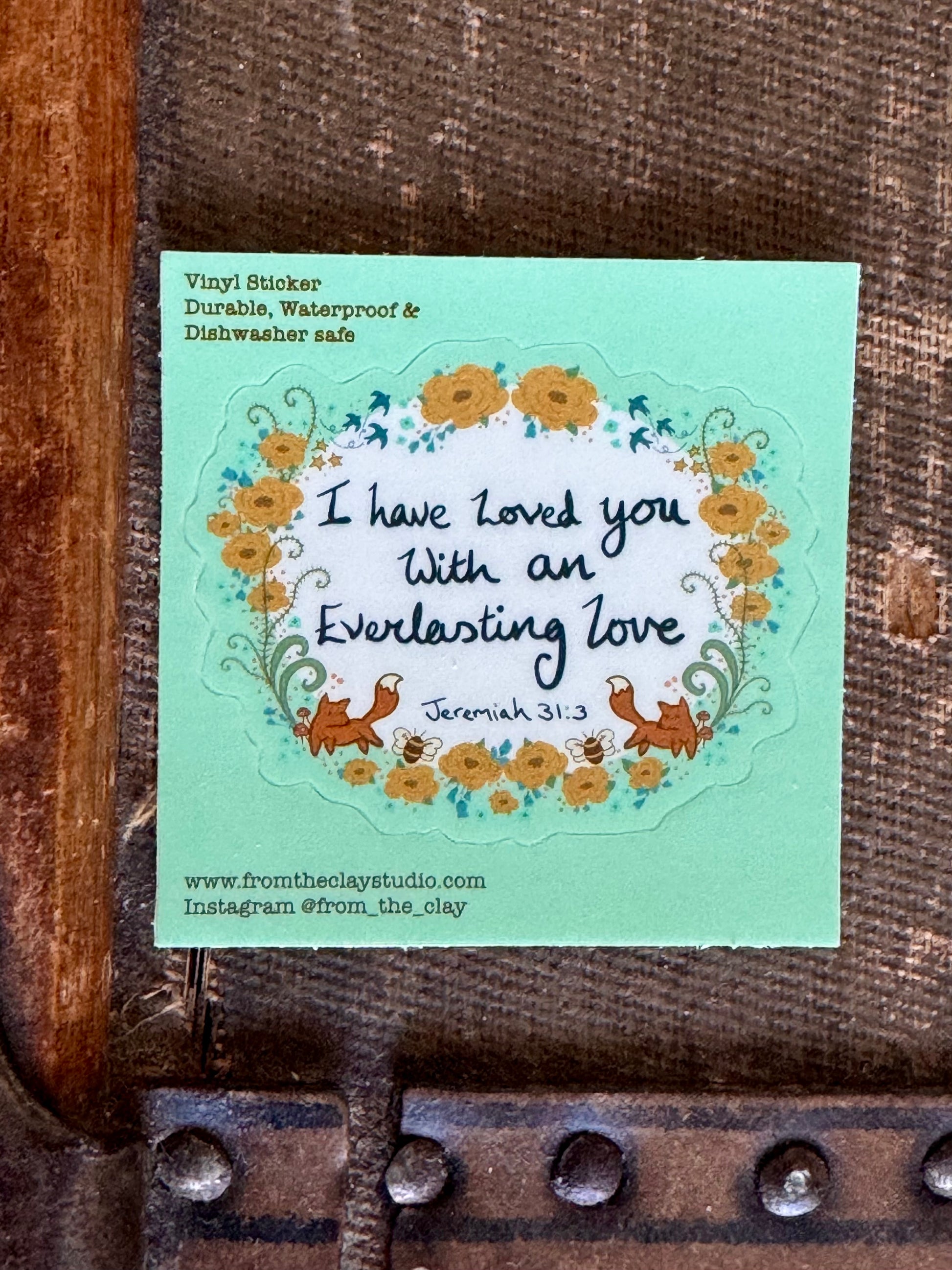 Vinyl sticker with the scripture I have loved you with an everlasting love written on the sticker, surrounded by a floral design of little mustard colored flowers and two foxes looking at each other