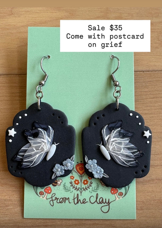 Black earrings with butterflies and small flowers on a green card with 'From the Clay' branding.