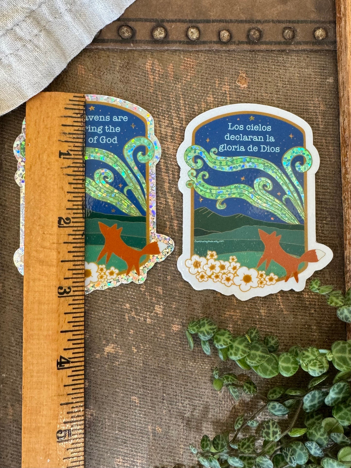 two stickers with fox looking at the northern lights at night with a ruler showing that they are 3" tall